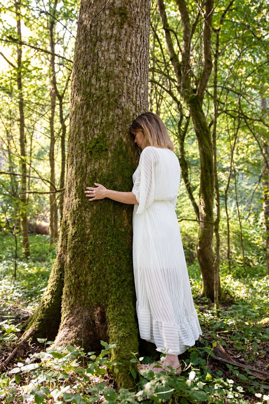 Femme posant la main sur un arbre moussu en forêt, symbole d'ancrage et de connexion à la nature